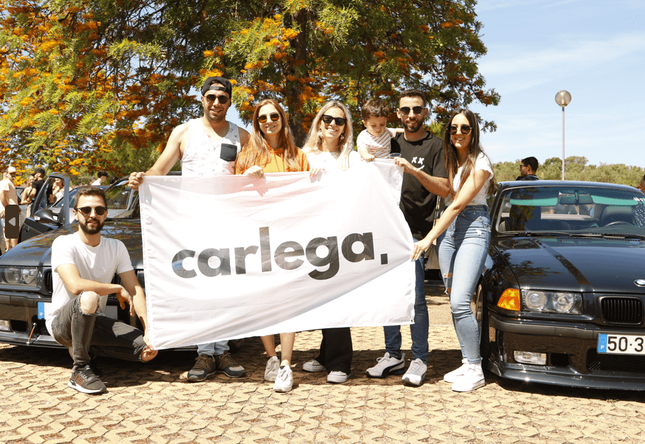 Grupo de clientes Carlega a segurar a bandeira da marca num encontro de carros