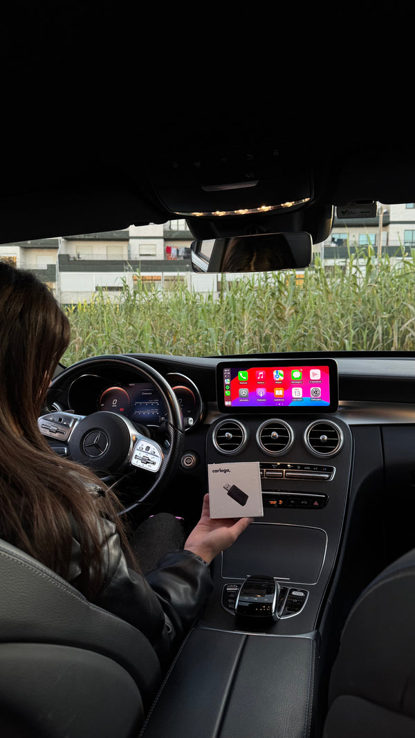 Condutora a segurar a Pen Carlega dentro de um Mercedes à noite, com o CarPlay no ecrã
