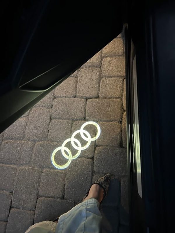 Logótipo da Audi projetado na calçada junto à porta de um carro