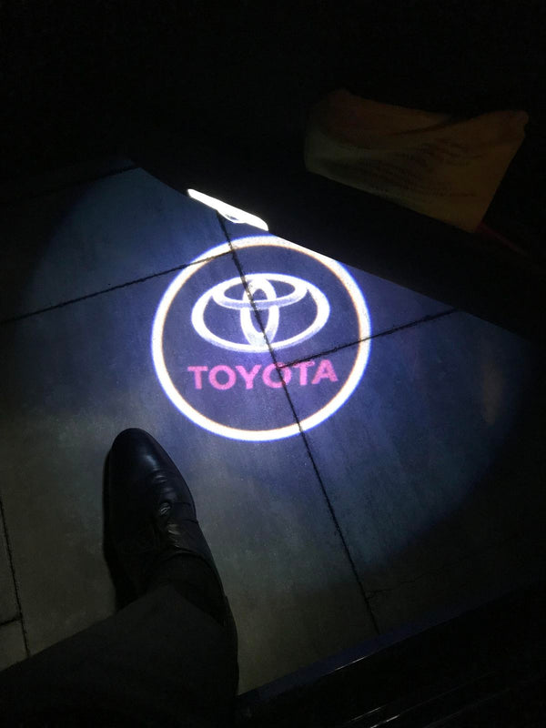 Logótipo da Toyota projetado no chão junto à porta de um carro, à noite